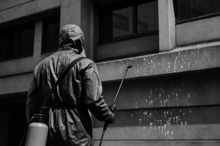 Silhouette d'un professionnel en combinaison nettoyant un bâtiment urbain des fientes de pigeons.